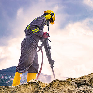 An industrial worker operating a drill on a rock pile, representing mineral and surface rights in Texas.
